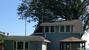 A two-story house with a porch and a large tree in front.