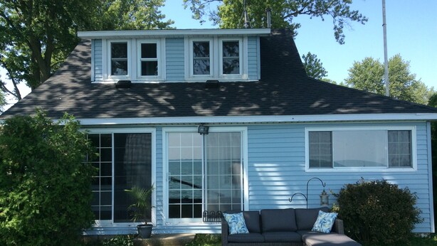 A two-story house with a covered porch, large sliding glass doors, and a dark-colored outdoor seating area.