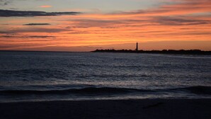 A coastal sunset with a lighthouse silhouette on a rocky outcrop. - Heart of Jackson St-4BR Victorian Unit just steps to Beach and Mall with Parking (Cape May)