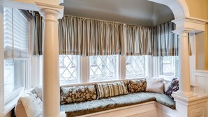 A bay window with a cushioned bench, white columns, and patterned curtains. - Heart of Jackson St-4BR Victorian Unit just steps to Beach and Mall with Parking (Cape May)
