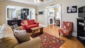 A living room with a red sofa, a beige sofa, a wooden coffee table, a patterned rug, and a ceiling fan. - Heart of Jackson St-4BR Victorian Unit just steps to Beach and Mall with Parking (Cape May)