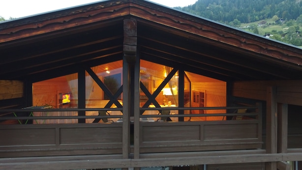 Une cabane en bois dotée d’un balcon, de grandes fenêtres et offrant une vue sur la forêt environnante.