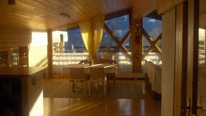 Un chalet confortable avec un intérieur en bois, un coin repas et de grandes fenêtres donnant sur le paysage extérieur.