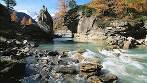 Un lit de rivière rocheux aux eaux claires, bordé d’arbres aux couleurs automnales et avec des montagnes en arrière-plan.