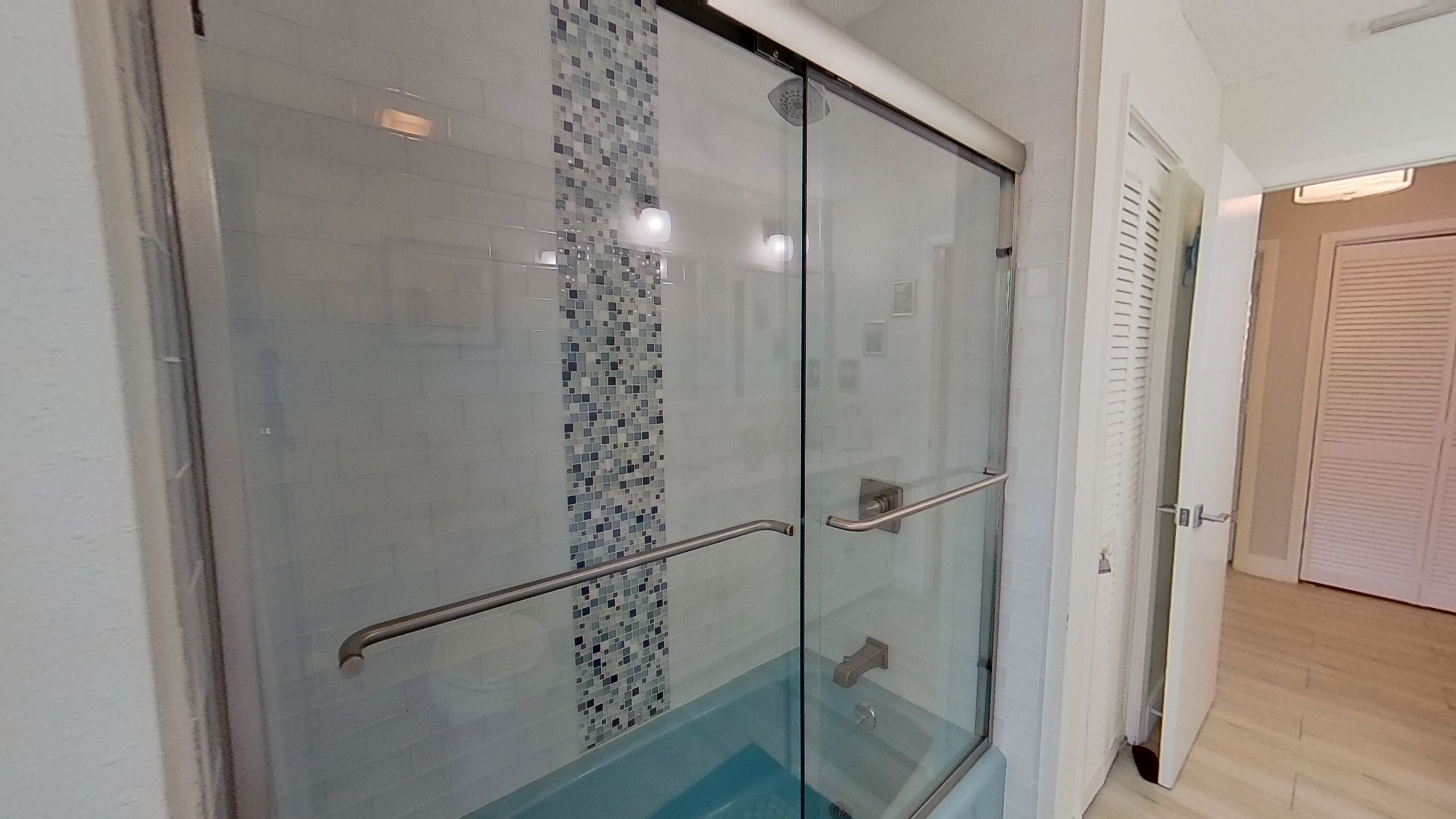 A glass-enclosed shower with a tiled mosaic wall, a glass door, and a metal handle.