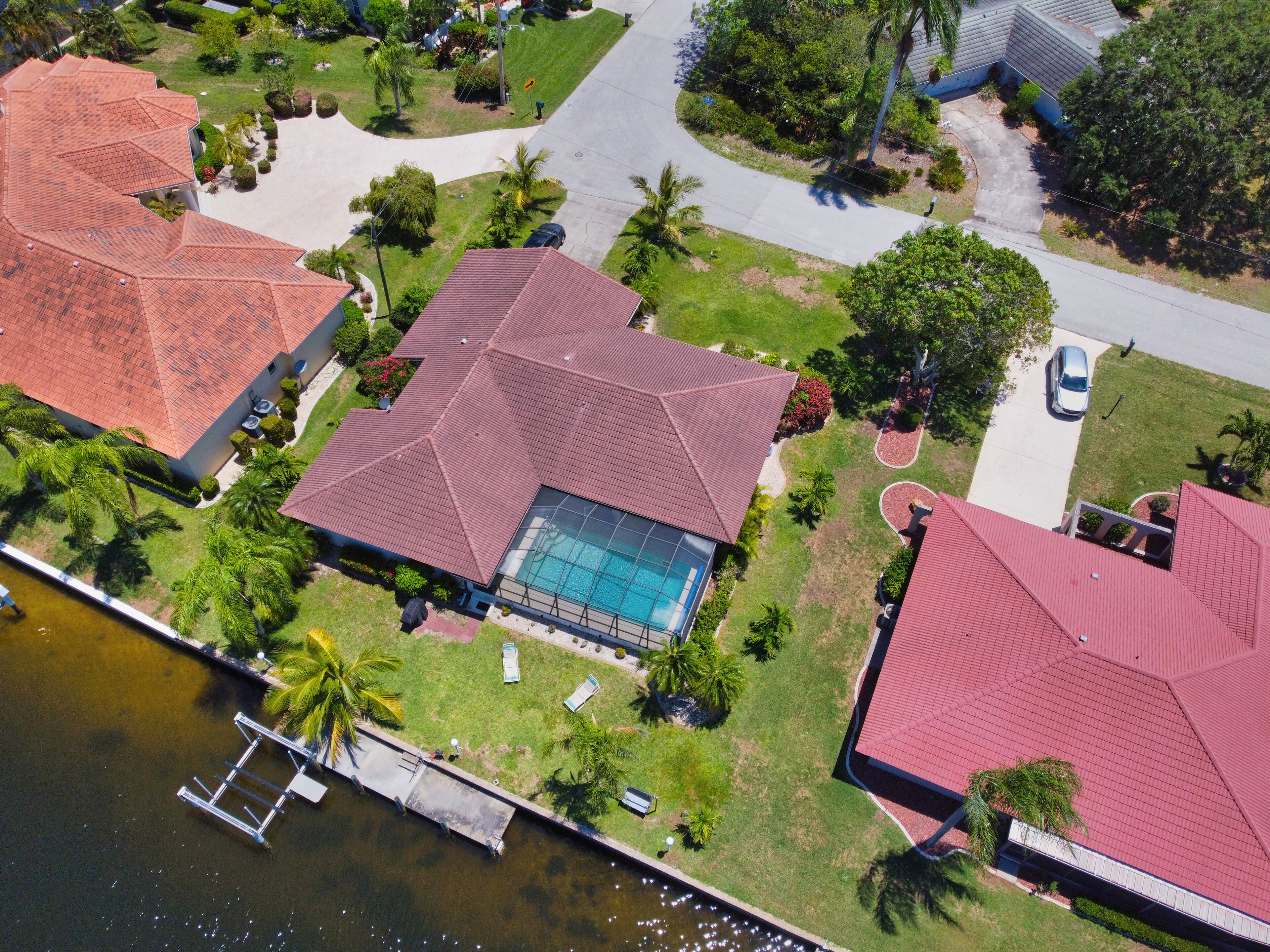 An aerial view of a residential property with a swimming pool, red-roofed houses, and a dock by a body of water.