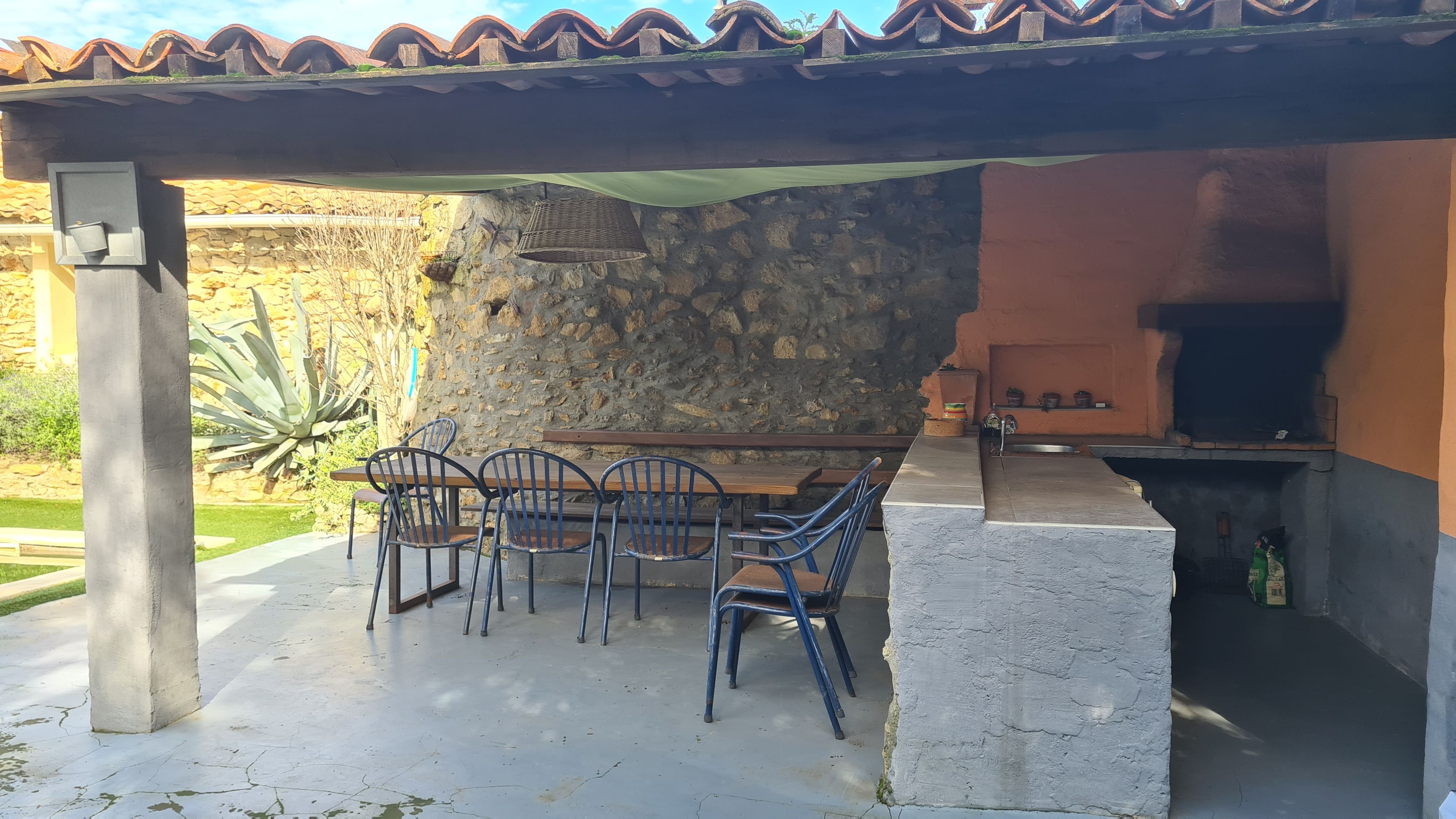 An outdoor patio with a stone wall, a wooden table, and metal chairs.