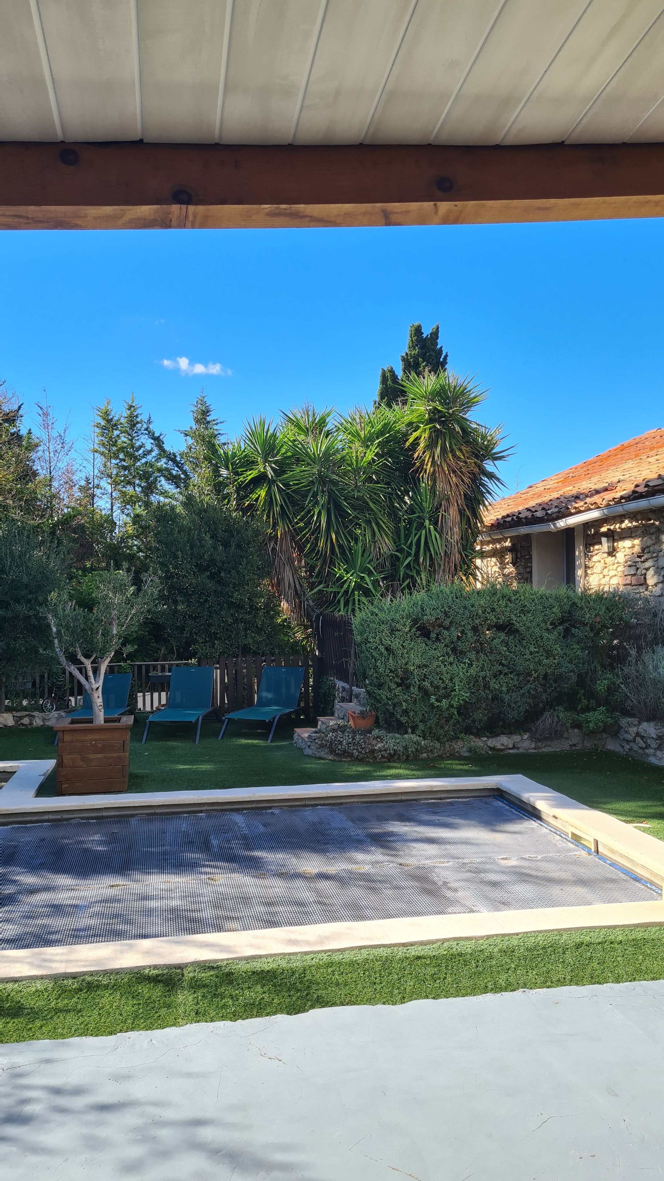 A pool area with a clear blue sky, surrounded by greenery and a stone building.