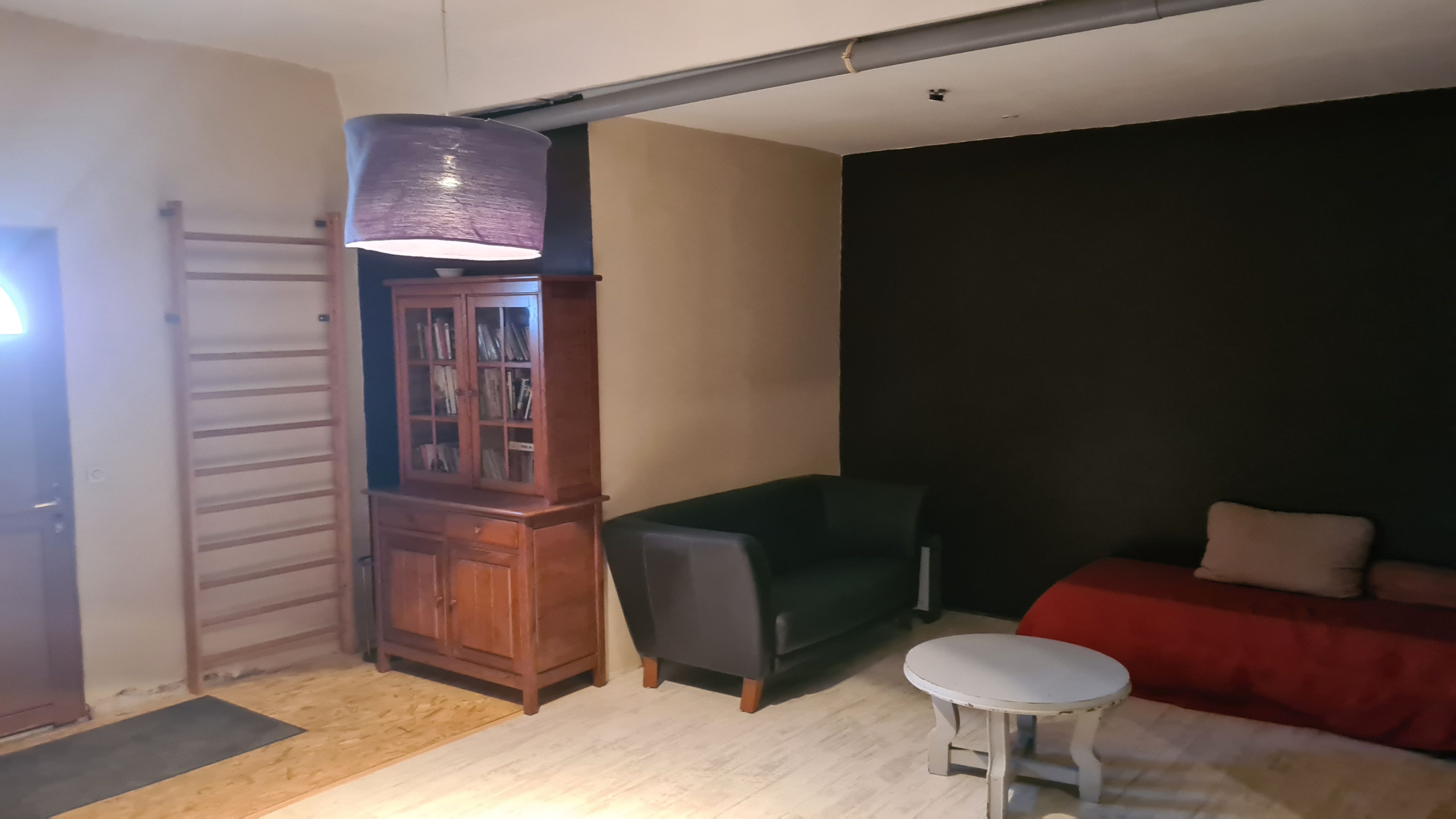 Una habitación con un armario de madera, un sofá verde, una mesita blanca y una pared de color oscuro.