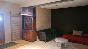Ein Zimmer mit einem Holzkabinett, einem grünen Sofa, einem kleinen weißen Tisch und einer dunkel gefärbten Wand.