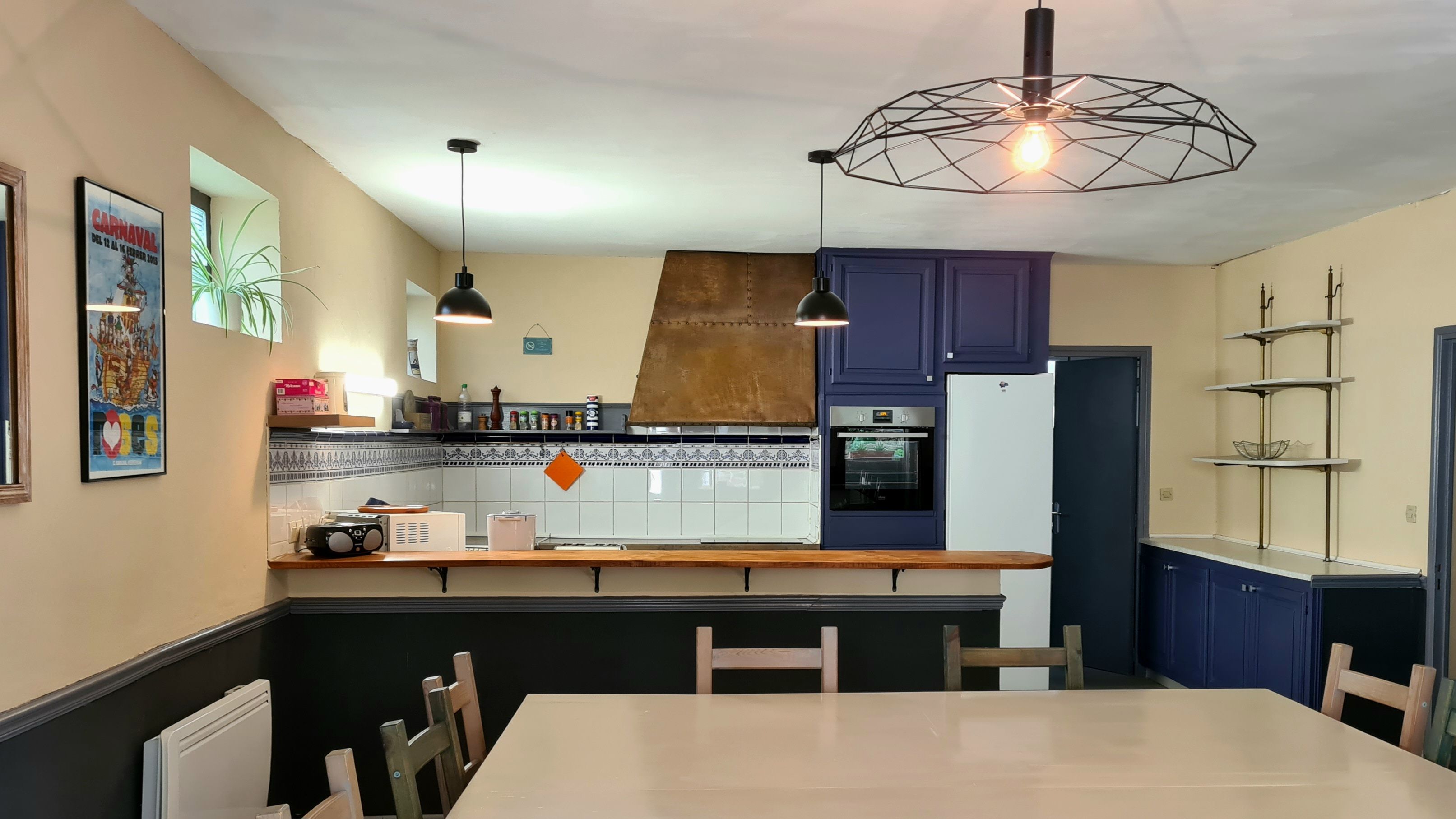 A kitchen with a wooden countertop, a built-in oven, and a refrigerator. There are two pendant lights and a geometric ceiling light fixture.