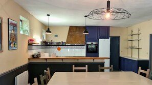 Eine Küche mit einer Holz Arbeitsplatte, einem eingebauten Backofen und einem Kühlschrank. Zwei Pendelleuchten und eine geometrische Deckenleuchte sind vorhanden.