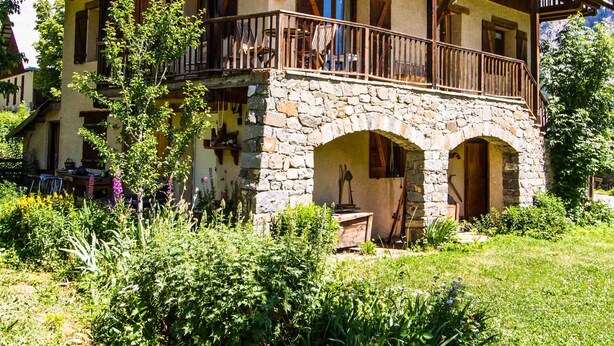 Un chalet traditionnel doté d’une entrée en arc de pierre, de balcons en bois et d’un jardin luxuriant.