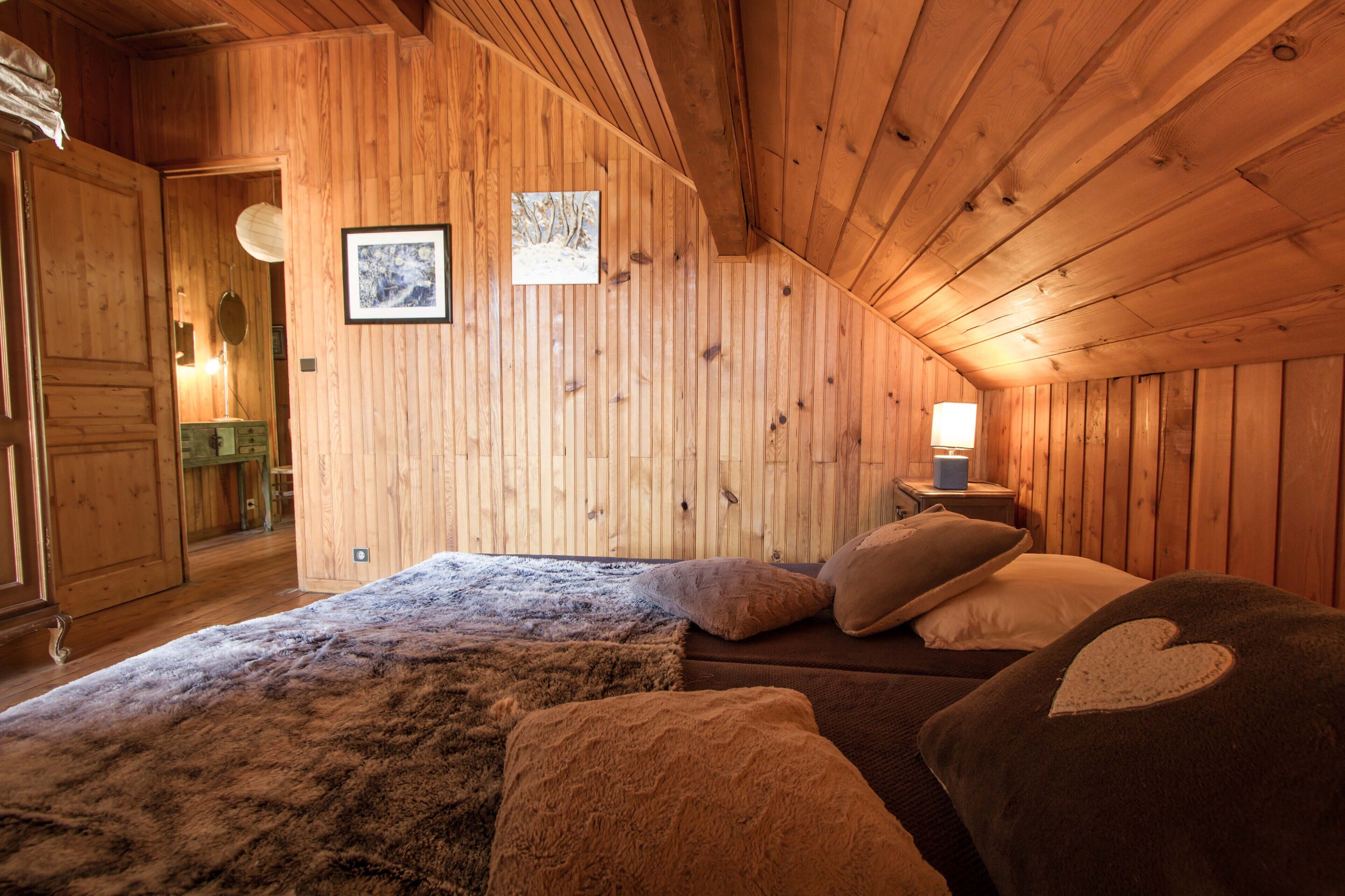 A cozy wooden cabin bedroom with a bed, pillows, and a nightstand with a lamp.