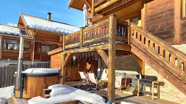 Een houten chalet met een hottub, buitenmeubels en een stenen muur.