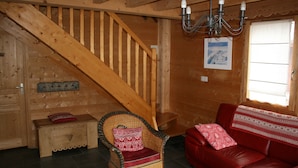 Een houten interieur met een trap, een rieten stoel, een rode leren bank en een houten kist.