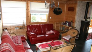 Een gezellige woonkamer met een rode leren bank, een rieten fauteuil en een houten salontafel.