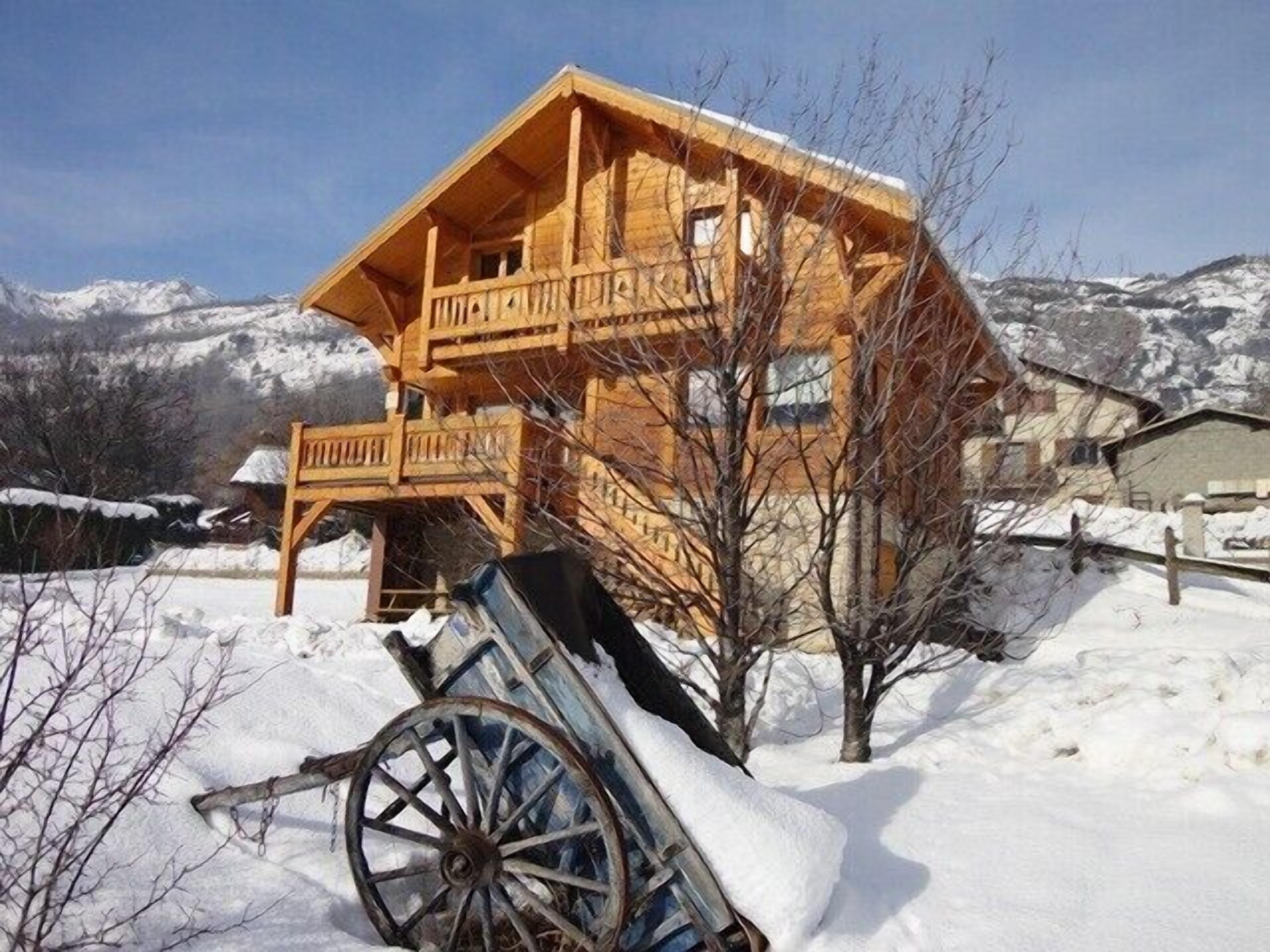 Een houten chalet met balkon, omgeven door sneeuw en bergen.