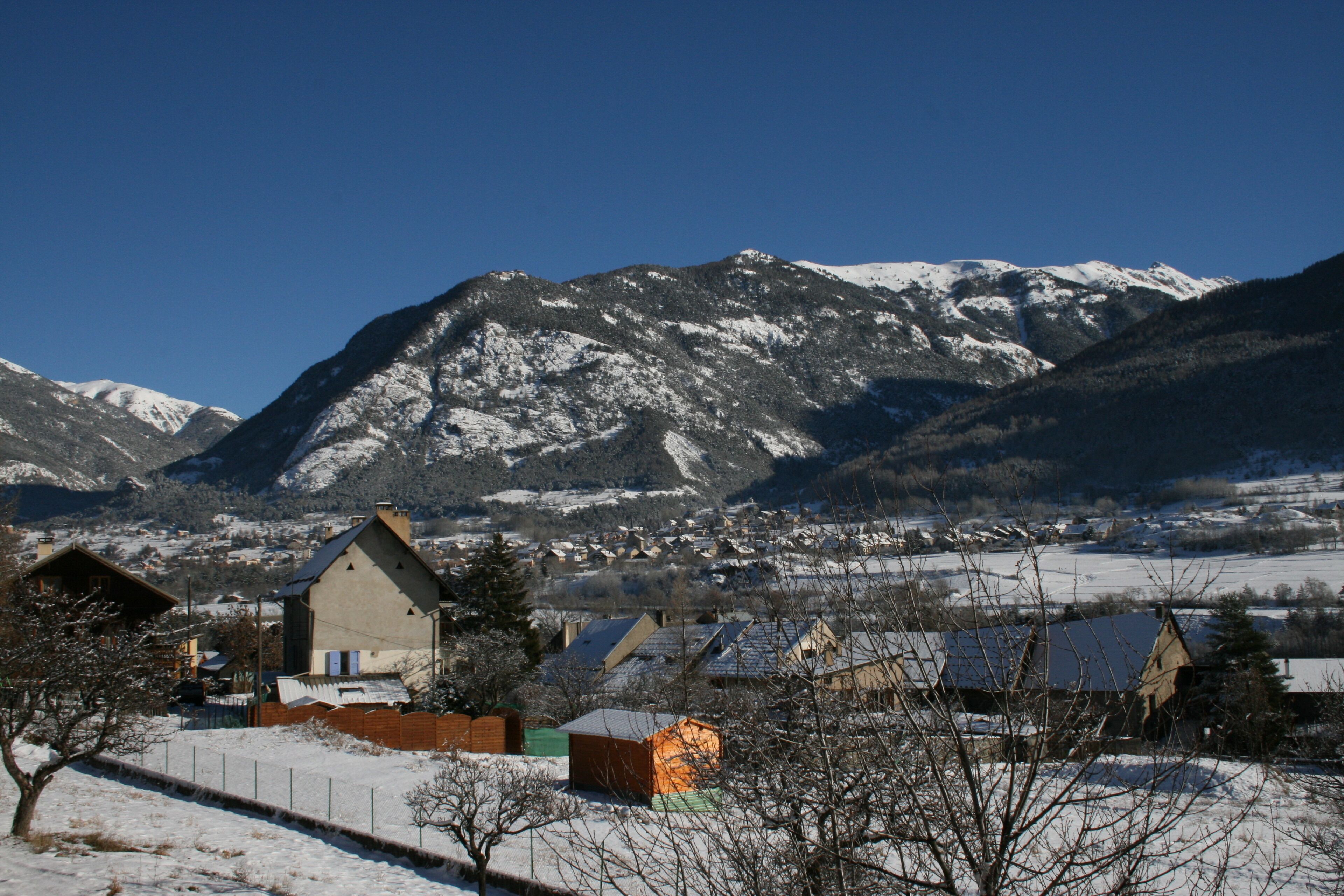 Un village enneigé, avec des maisons et une montagne en arrière-plan.