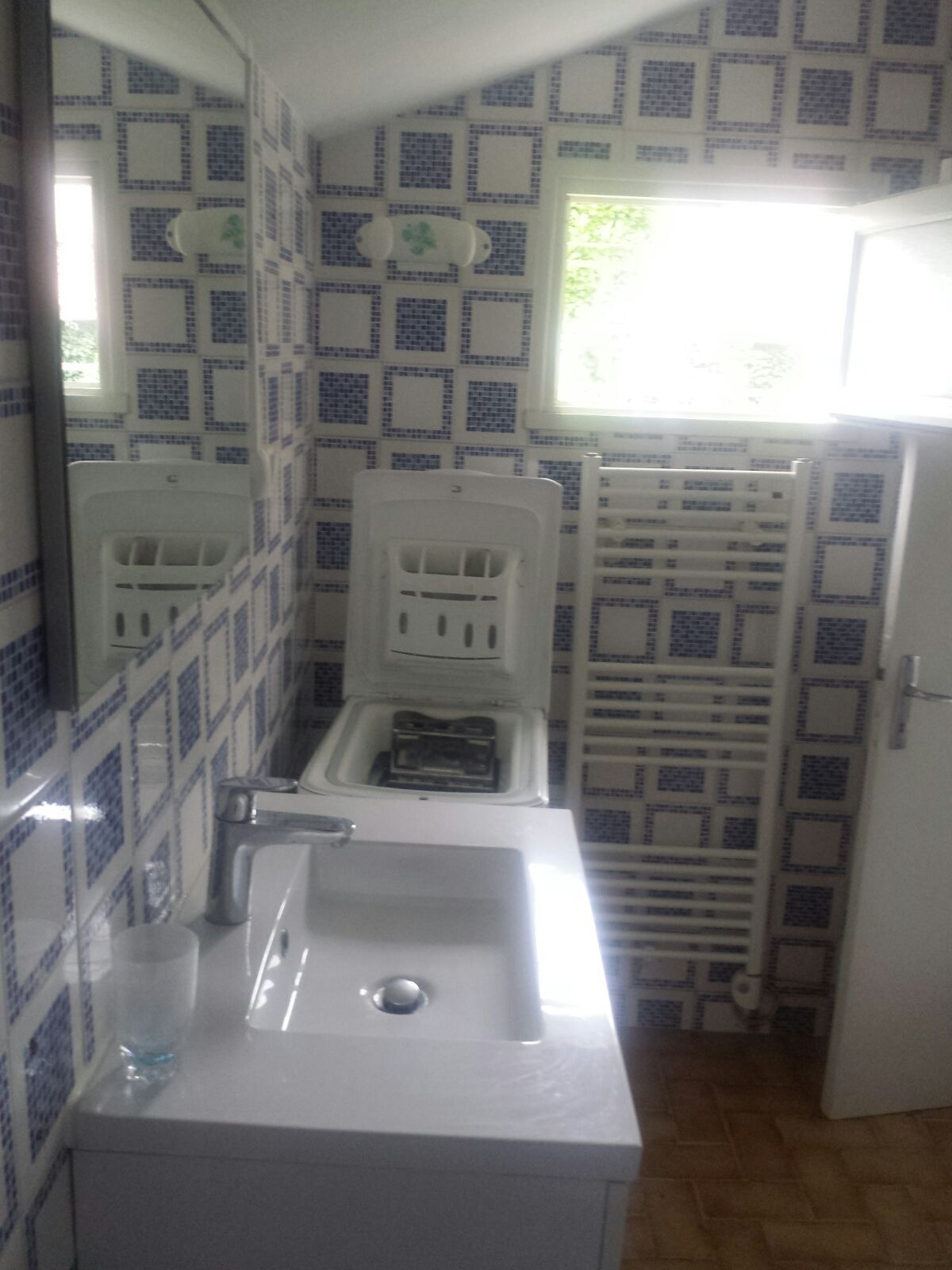 A bathroom with a white sink, a mirror, and a toilet. The walls have a blue and white patterned tile design.