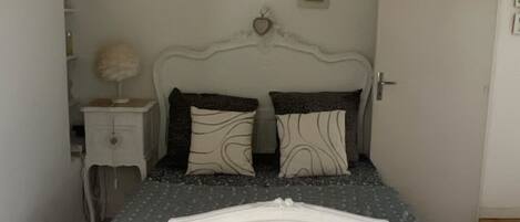 A bedroom with a white ornate bed, a nightstand with a lamp, and a door.