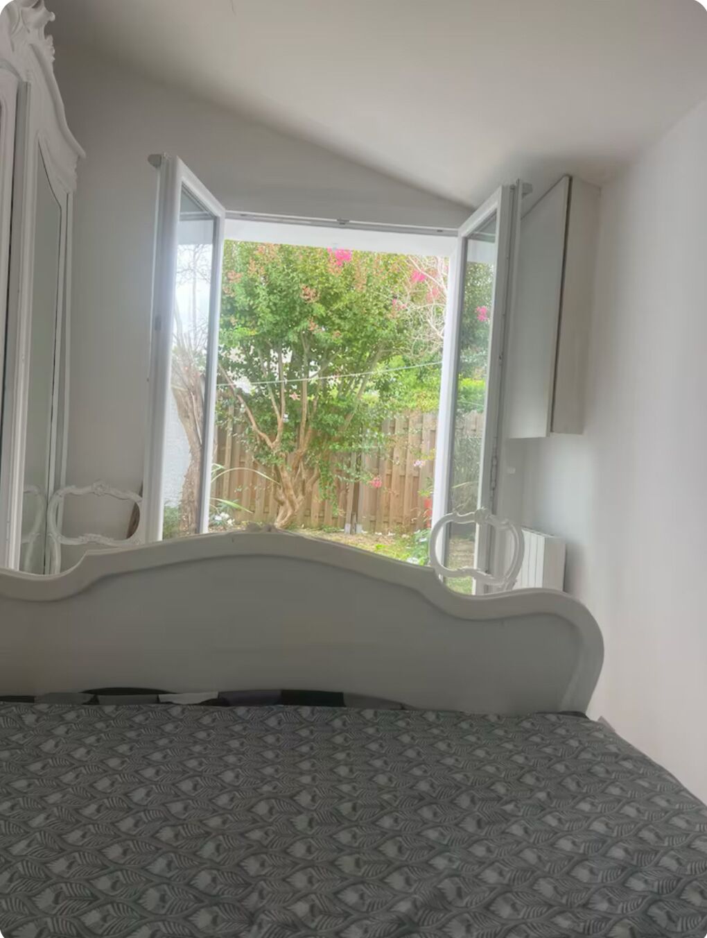 A bedroom with a bed, a window, and a view of a garden.