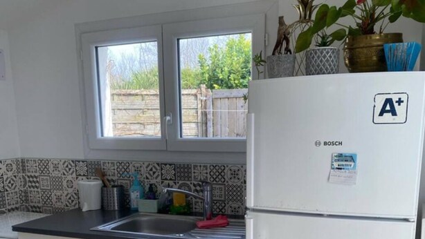 Een keuken met witte kastjes, een Bosch koelkast, een raam en een betegelde spatwand.