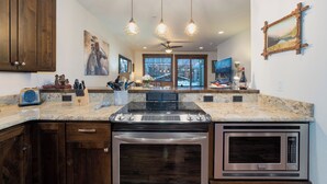 Eine moderne Küche mit Einbauherd, Backofen und Mikrowelle, Holzschränken und Pendelleuchten.