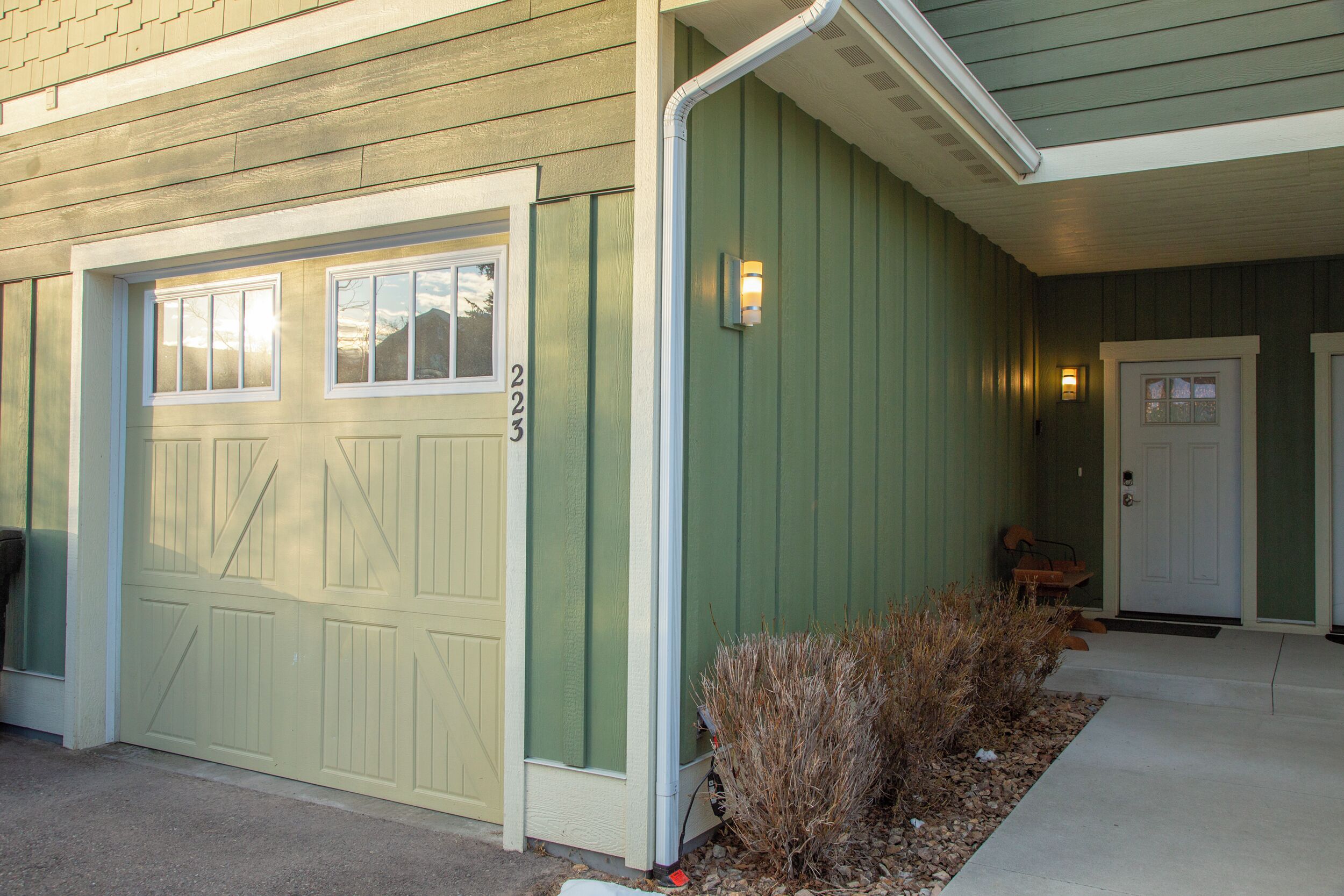 A house with a garage door, a mailbox, and a door with a number plate.