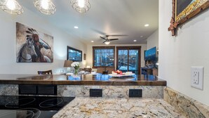 Eine moderne Küche mit Granit Arbeitsplatten, einem eingebauten Herd, Pendelleuchten und einem großen Gemälde an der Wand.