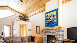 Un salon chaleureux avec une cheminée en pierre, un ventilateur de plafond et un grand tableau accroché au mur.