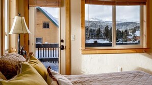 Une pièce confortable avec un lit, une lampe et une fenêtre donnant sur un paysage enneigé et un chalet en bois.