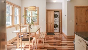 A modern kitchen with wooden flooring, a dining area with a table and chairs, and a built-in washer and dryer. - Epic Views! Immaculate Modern Cabin Just 10 Min. From Downtown! (Asheville)