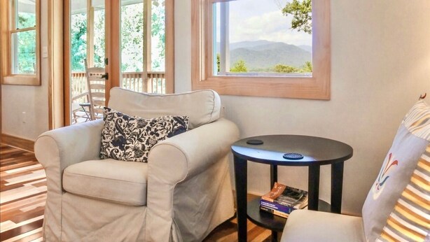 A room with a sofa, a small table, and a view of a deck and mountains. - Epic Views! Immaculate Modern Cabin Just 10 Min. From Downtown! (Asheville)