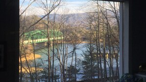 A view through a window of a green bridge over a body of water, surrounded by trees and mountains.