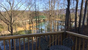 A wooden deck with a metal table and chairs, overlooking a river and a bridge.