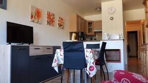Una cocina compacta con televisión, una mesa de comedor con sillas y un reloj en la pared.