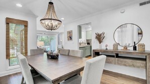 Un espace repas comprenant une table en bois, des chaises rembourrées, un lustre et un grand miroir posé sur une console en bois.