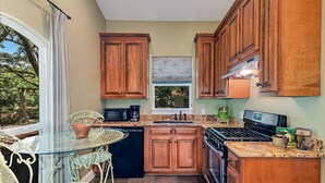 A kitchen with wooden cabinets, a gas stove, a dishwasher, and a window overlooking greenery. - Farm Stay: Come Stay With Us (Fairhope)
