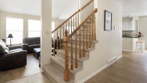 A spacious living room with a large sectional sofa, a wooden staircase, and a kitchen area in the background.