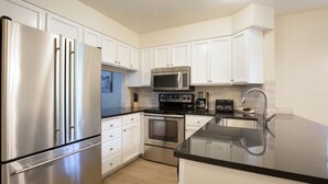 A modern kitchen with stainless steel appliances, white cabinetry, and a black countertop.