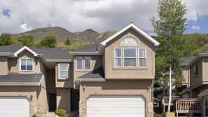 A suburban two-story house with a garage, a small front yard, and a mountain in the background.
