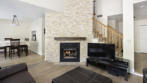 A modern living room with a stone fireplace, a flat-screen TV, and a staircase.