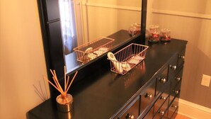 Een zwarte dressoir met twee draadmanden erbovenop, een spiegel en een klein vaasje met rietstengels.