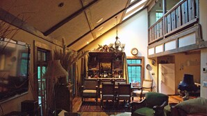 A cozy living room with a fireplace, a dining area with chairs, a chandelier, and a view of the outdoors through a window. - Luxurious, rustic, private vacation home with great view. (Davis)