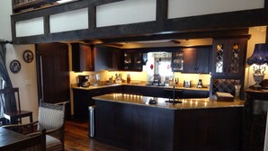 A kitchen with dark wooden cabinets, a large island, and a dining area with a chair and table. - Luxurious, rustic, private vacation home with great view. (Davis)