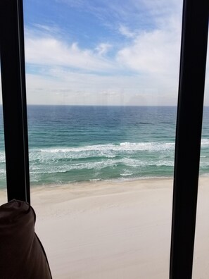 A view of the ocean through large windows, with a sandy beach visible in the foreground. - Edgewater Beach & Golf Resort, Ocean Front, 2 BR, 2 Bath (Panama City Beach)