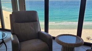 Une pièce dotée d’une grande fenêtre donnant sur une plage, d’un fauteuil en cuir et d’une table en osier.