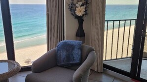 Un balcon donnant sur la plage, un fauteuil gris avec un plaid bleu et un vase rempli de fleurs.