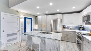 A modern kitchen with a central island, stainless steel appliances, and white cabinetry. - Coquina Beach 3G- Gorgeous 2bd, plus loft, Sanibel beach condo! (Sanibel)